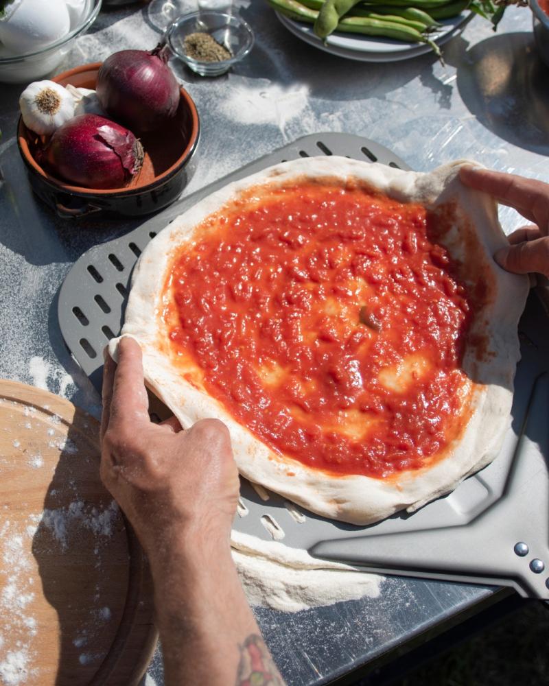 Homemade pizza is being prepared to be baked using the right pizza dough ingredients and tools.