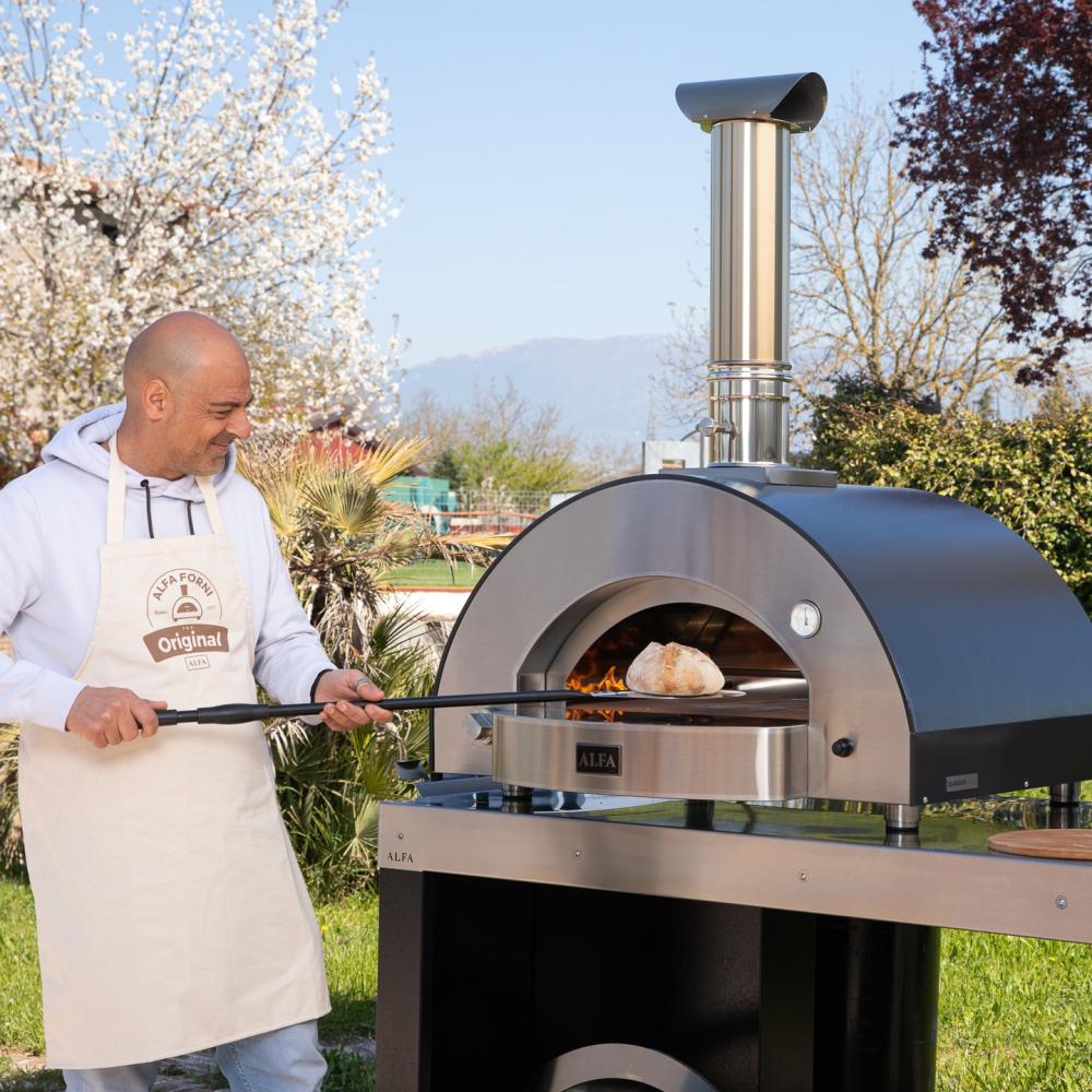 Wood-burning oven with a man baking bread using Alfa Forni oven outdoors.