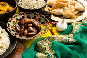  A vibrant arrangement of Middle Eastern dishes includes samosas, dates, rice, curry, and spices. A green embroidered fabric adds a cultural touch.