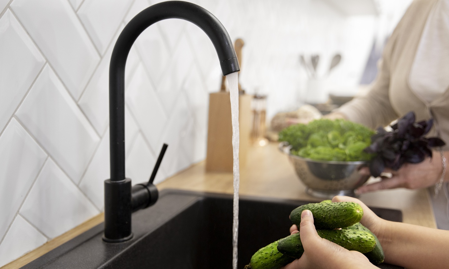 Washing vegetables using a black kitchen mixer tap complements black sink.