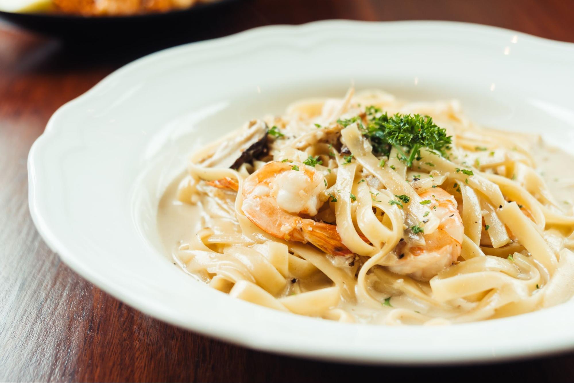 A bowl of creamy garlic shrimp pasta, topped with herbs and served with a side of toasted bread.