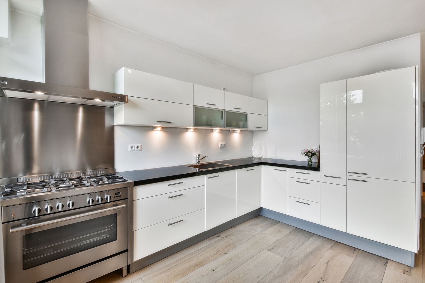 Modern kitchen with sleek white cabinets, a stainless steel oven and hood, light wood flooring, and soft under-cabinet lighting, creating a clean, bright atmosphere.