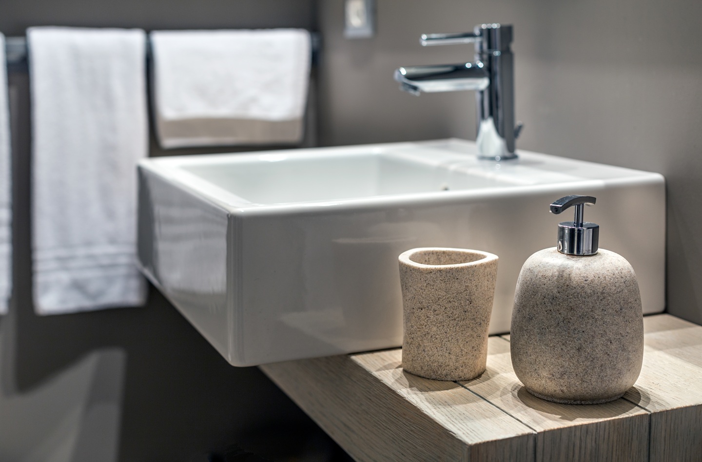 Compact wash basin mixer for bathrooms with a stainless steel finish over a white porcelain sink. 